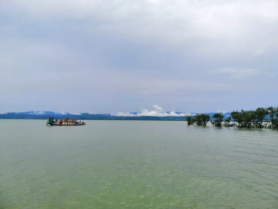 Boat with travelers in Tanguar haor, trees, and clouds