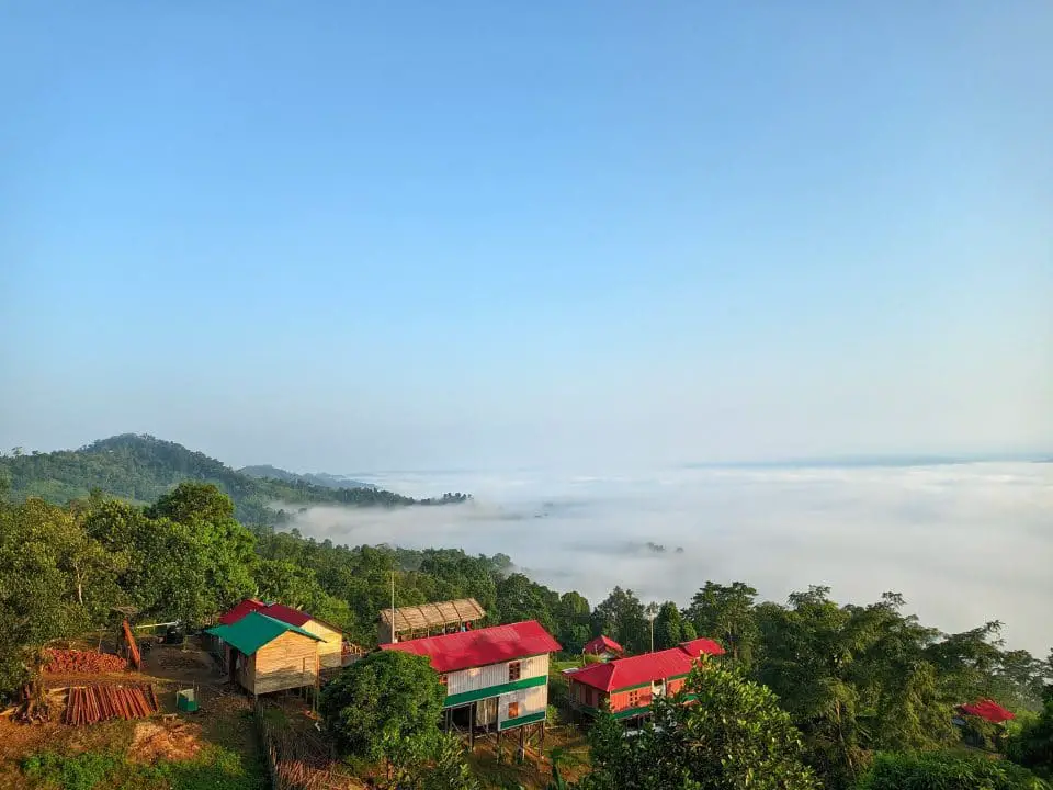 Majestic View of Sajek Valley in Bangladesh. Lots of colorful house, tons of white clouds covered a part of the place, and green trees in another part.