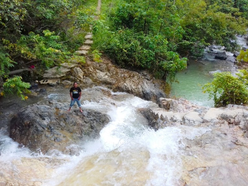 A man is standing in Seventh Level Waterfall/Air Terjun .Tingkat Tujuh. Its a Top-Rated Tourist Attractions In South Aceh.