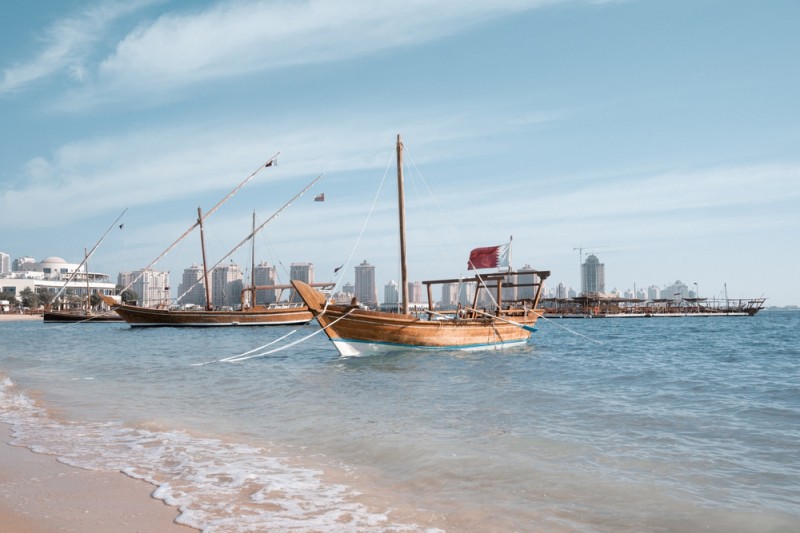 Three wooden boats on a sandy beach, with a cityscape in the background